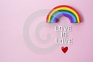 LGBT pride concept. Text LOVE IS LOVE with rainbow over pink background, top view. Copy space