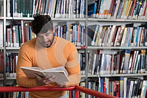 Happy Male Student Reading from Book in Library