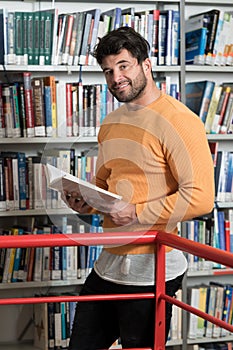 Happy Male Student Reading from Book in Library