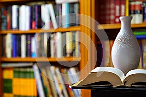 library with many books to read, arranged on shelves. Open book and vase in the foreground. Copy space