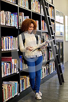 The librarys the best place to study. a young woman studying from a book while standing by a library bookshelf. photo