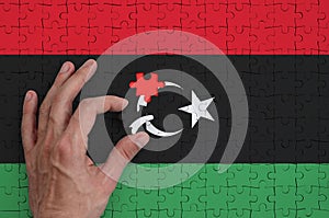 Libya flag is depicted on a puzzle, which the man`s hand completes to fold