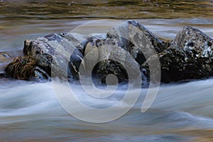 Lichen covered rock formation surrounded by swiftly running waters