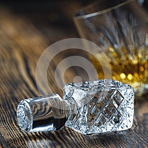 lid from a crystal decanter close-up on a wooden table. a glass of whiskey in the background