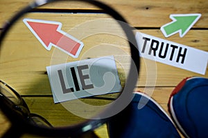 Lie or Truth opposite direction signs in magnifying with sneakers and eyeglasses on wooden