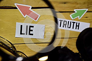 Lie or Truth opposite direction signs in magnifying with sneakers and eyeglasses on wooden