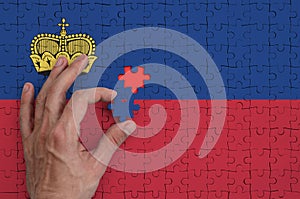 Liechtenstein flag is depicted on a puzzle, which the man`s hand completes to fold