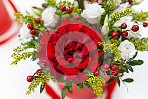 Life-affirming composition of fresh flowers Rose, Eustoma, Solidaga, Pistachio leaves and decorative berries in a scarlet cardbo