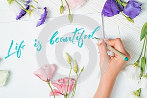 Life is beautiful text. Font of lettering word on white paper with green ink by calligrapher. Flowers frame. Graphic