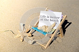 LIFE IS BETTER AT THE BEACH text on paper greeting card on background of beach chair lounge starfish summer vacation