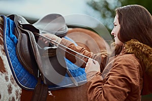 Life is better with a pony. a teenage girl preparing to ride her pony on a farm.