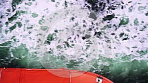 Life boats and wake water from a cruise ship at sea seen from the side of the ship while sailing.