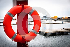 Life buoy attached to metal post on a pier with ships on the background. Safety