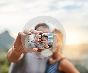 Life is a collection of memories. Portrait of a happy young couple taking selfies on a phone outdoors.