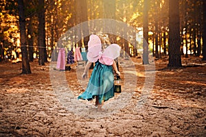 This is the life of a fairy. an unrecognizable little girl holding a lamp while running around outside in the woods.