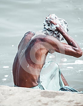 Life on the Ganges. Poor man of low caste washing himself with soap foam in the dirty waters of the river Ganges