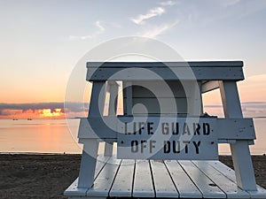 Life guard off duty sign on wooden beach chair winh sunrise