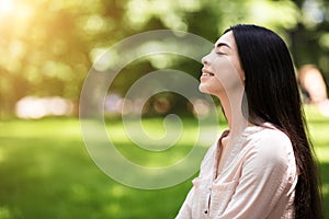 Portrait of relaxed asian girl breathing deeply with closed eyes in park photo