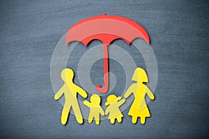 Life insurance concept. Paper cutout of family father, mother, son and daughter under red umbrella on blackboard background.