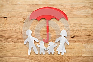 Life insurance concept. Paper cutout of family father, mother, son and daughter under red umbrella on wooden background.