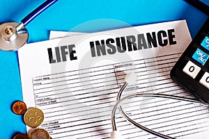 LIFE INSURANCE is written on the insurance policy next to the stethoscope, calculator and coins. Medical and insurance concept