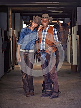 Life at the ranch. Shot of a cowboy and cowgirl leading a horse out of a stable.