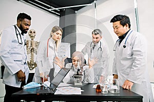 Life scientists researching in laboratory. Female Muslim young scientist microscoping and cheerfully gesturing while her