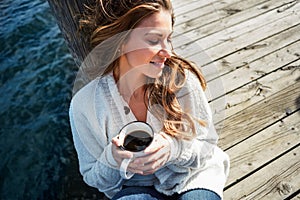 Life is simple - just add water. a beautiful young woman enjoying a warm beverage on a pier at a lake.