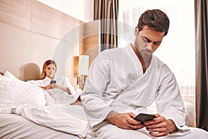 Life in smartphones. Couple are lying in hotel room bed