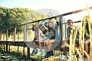 Life is sweet up the creek. Shot of a group of teenagers sitting on a bridge in nature at summer camp.