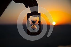 Life time passing concept. Hand holding hourglass with sunset sky background.