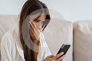 Life troubles, break up with boyfriend, bad news, heartbreak. Worried woman sitting on couch holds mobile phone read message