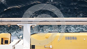 Lifeboat on giant cruise ship view down to ocean surface with waves below while ship cruising saling in the sea. safety muster