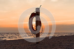 Lifebuoy on the beach against the background of an orange sunset over the sea