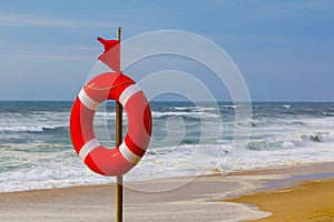 Lifebuoy and red warning flag flapping in the wind on the beach at storm. A symbol of the deterioration of the weather