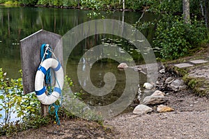 Lifebuoy and a rope are hanging on a special board, on the shore of a beautiful forest lake in which trees are reflected