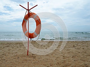 Lifebuoy on a sandy beach. Orange circle on a pole to rescue people drowning in the sea. Rescue point on the shore. Sky