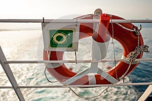 Lifebuoy with sign on a ferry fence, with sun and sea in backgro