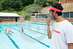 Lifeguard blowing whistle while students playing in pool