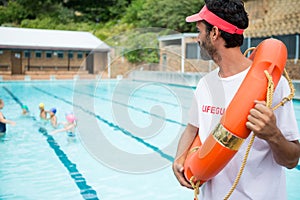 Lifeguard with lifebuoy looking at students playing in the pool