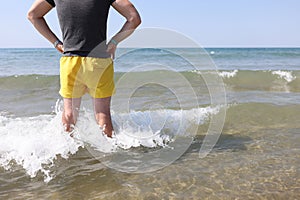 Lifeguard man in yellow shorts stands in sea water and looks into distance