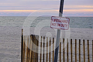 Lifeguard not on duty sign against gray ocean at sunset