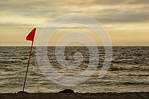 A lifeguard`s flag in the afternoon light of an overcast beach.
