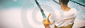 Lifeguard sitting on chair with rescue buoy at poolside