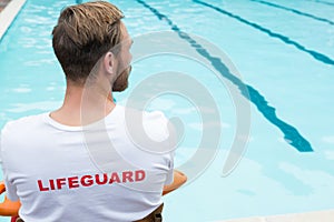 Lifeguard sitting on chair with rescue buoy at poolside