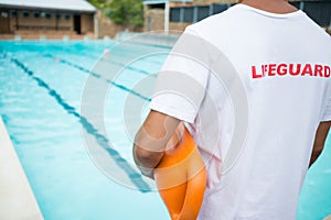 Lifeguard standing with rescue buoy near poolside