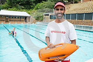 Lifeguard standing with rescue buoy near poolside