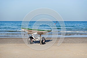 Lifeguard surf rescue surfboard with oars on the stand with wheels on sand beach close the sea.