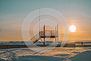 Lifeguard tower against the backdrop of sunset on a snow-covered beach in Parnu, Estonia