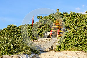 Lifeguard tower on the beach with green vegetation and blue sky background.